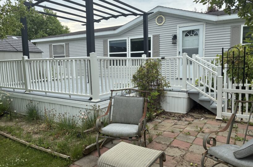 Patio area with three metal-frame chairs on a brick-paver surface, white railing, and a gray house with a porch door in the background.